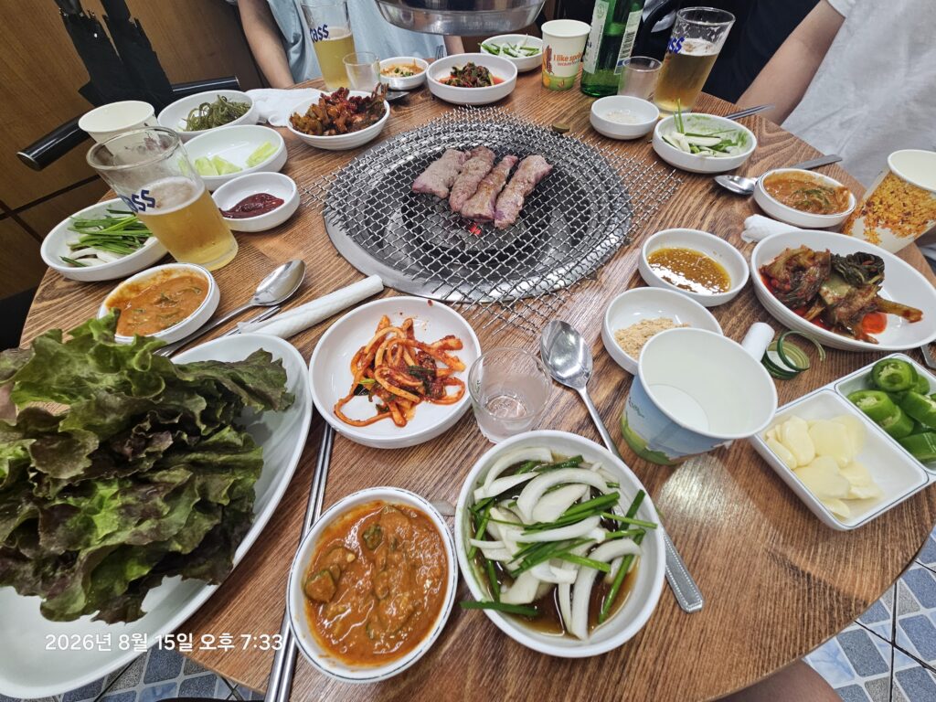 Korean BBQ table with grilled meat, side dishes, soju, and beer